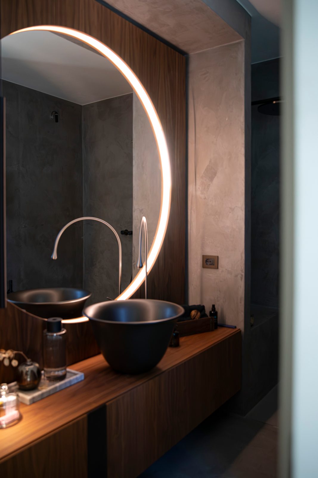 Bagno con pareti in microcemento, lavabo nero e specchio tondo retroilluminato