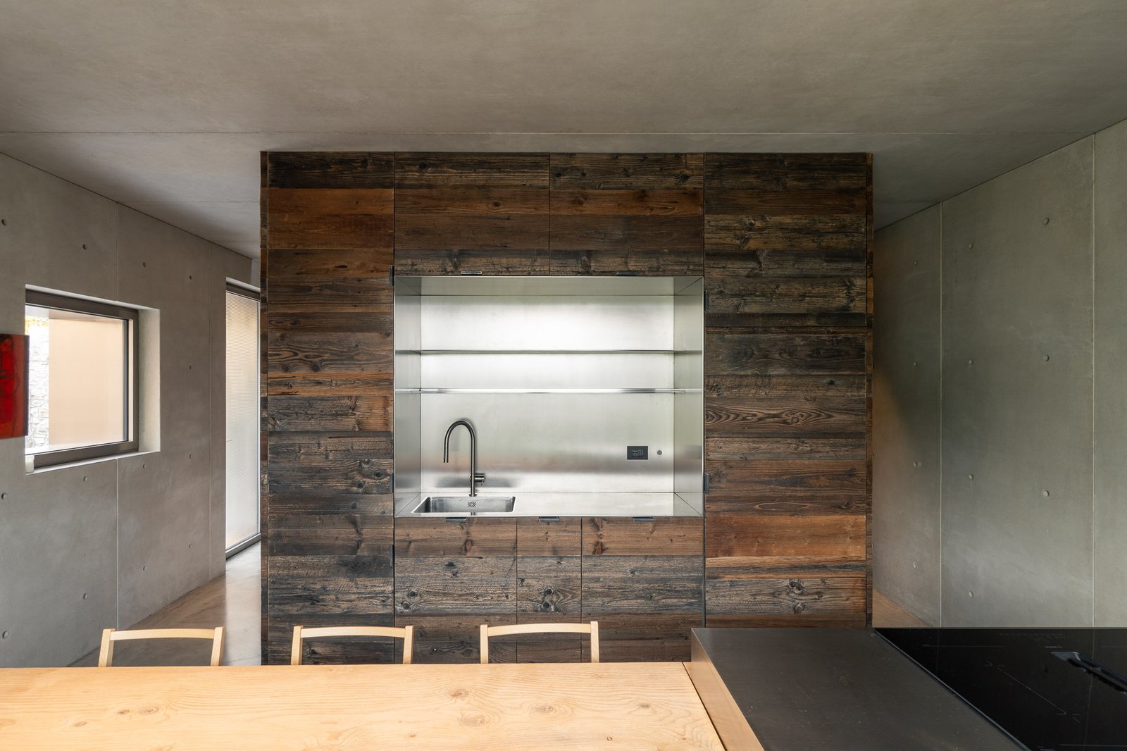 Cucina nel cubo in legno di recupero, pavimento continuo in cemento nuvolato, casa Vertigo a Brugnello