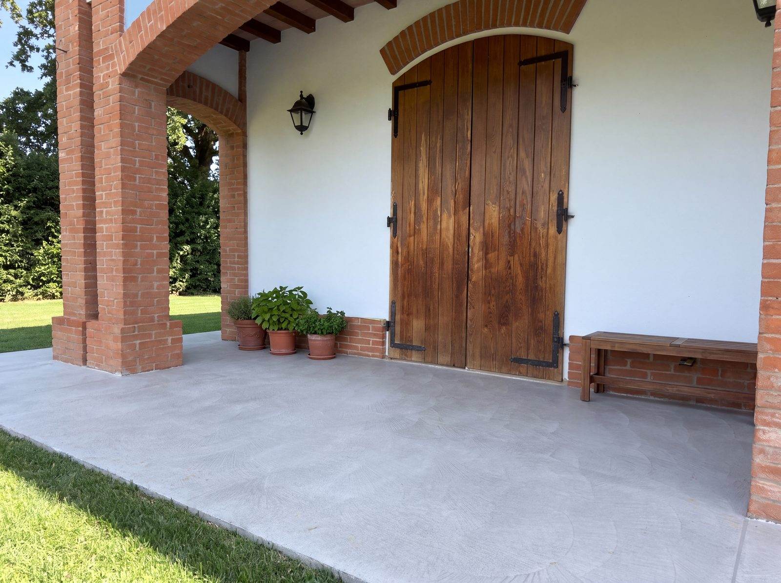 Portico di ingresso con portone in legno e pavimento in cemento Rasico a Novellara